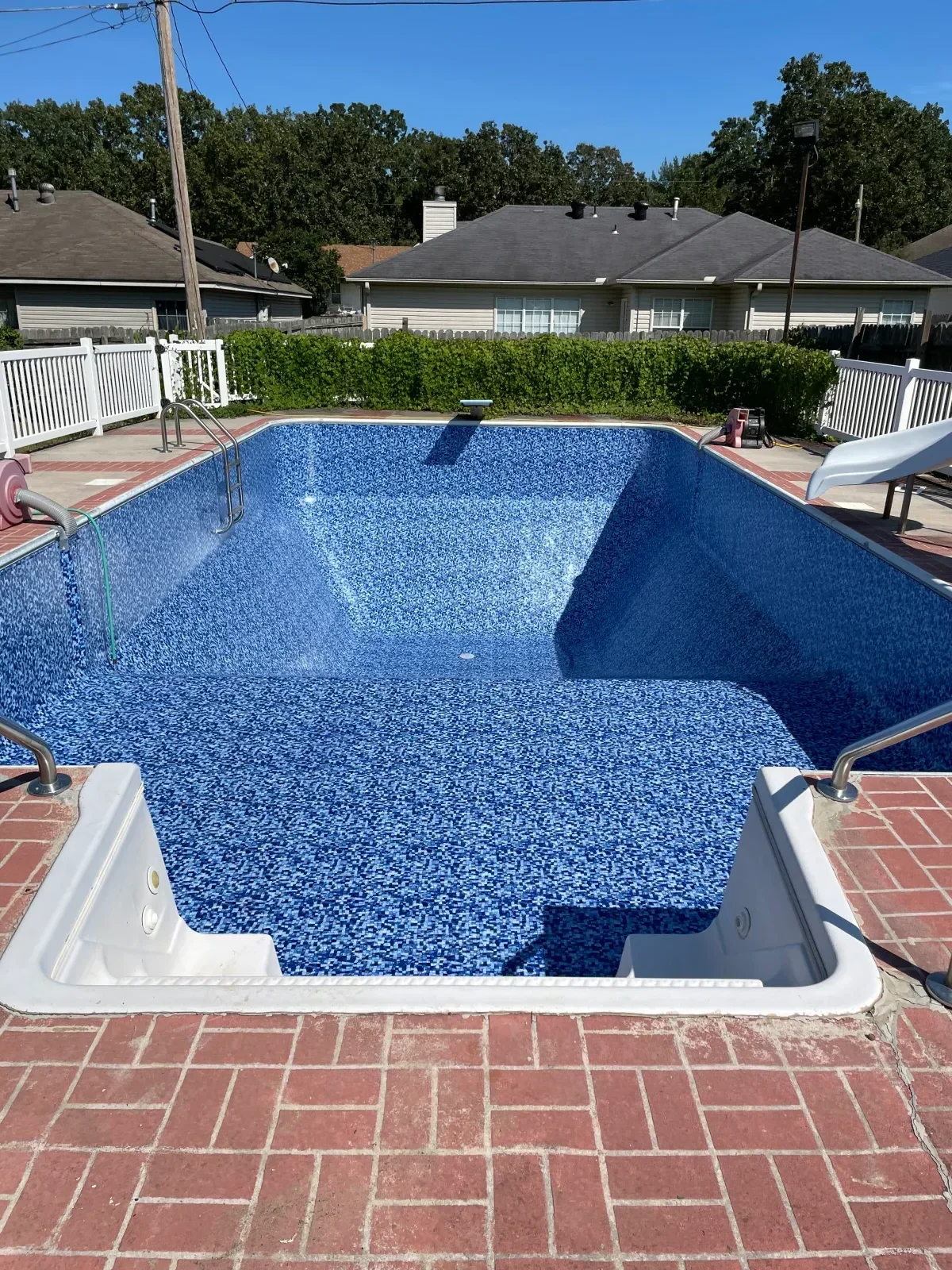 In-ground residential pool with blue pebble finish, white coping, and brick surroundings