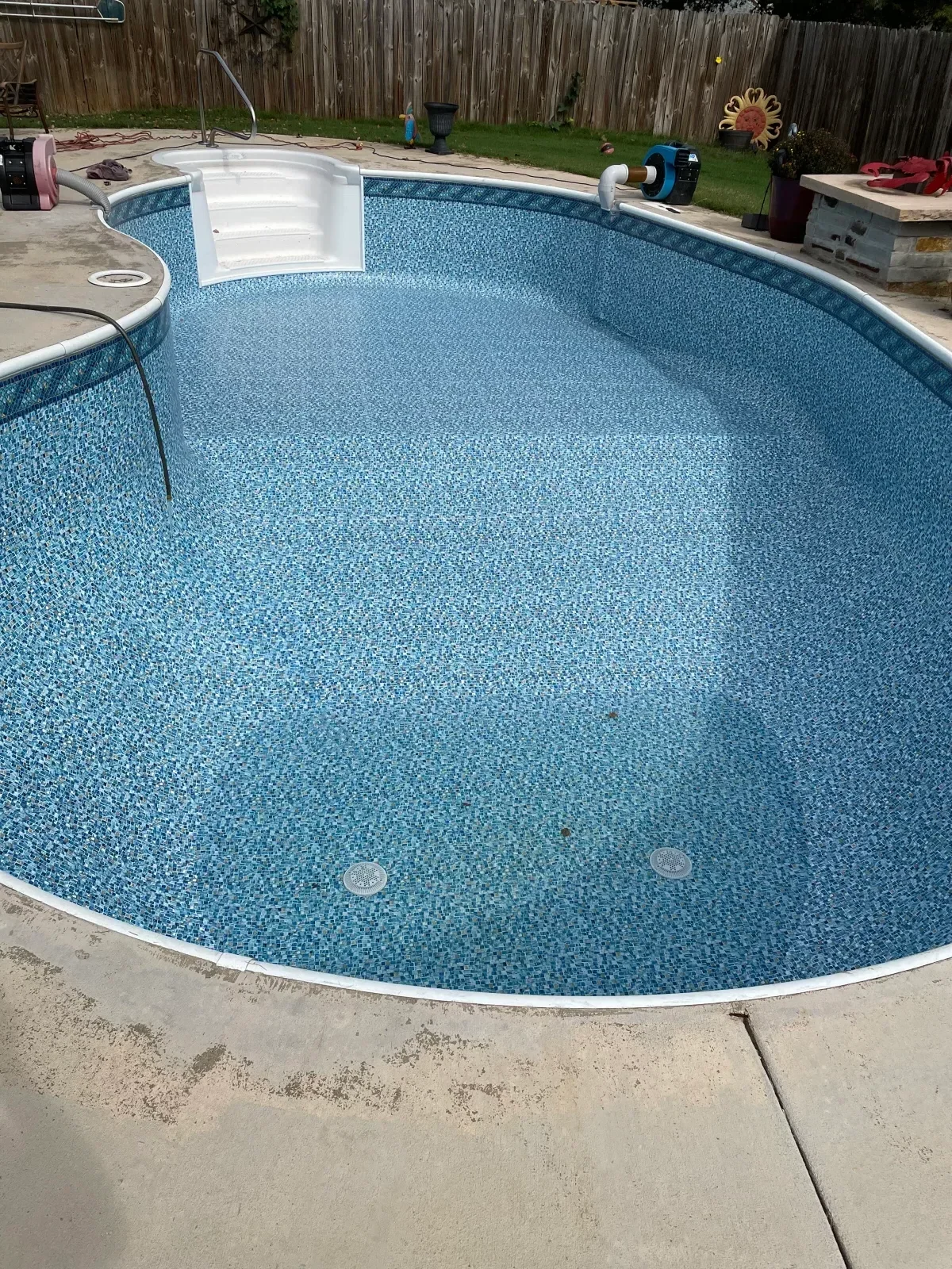 Above-ground pool with blue mosaic tile finish, white coping, and concrete deck surround
