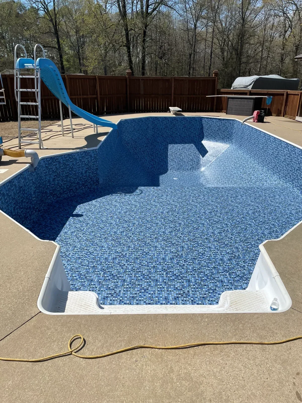 In-ground pool with blue mosaic tile interior, white coping, and blue slide installation
