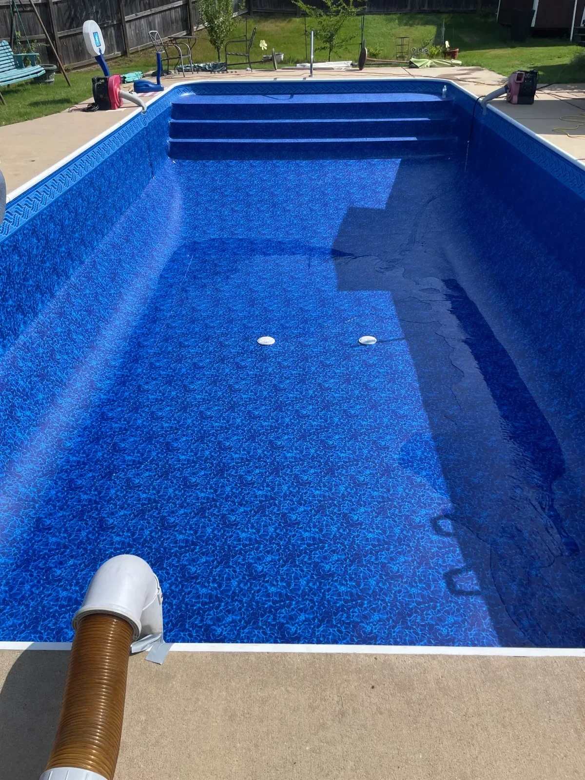 Blue vinyl pool liner installed on in-ground pool walls and floor with drainage pipe visible