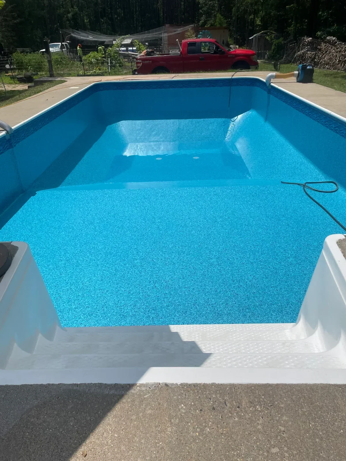 In-ground pool with bright blue plaster finish, white coping, and textured pool surface