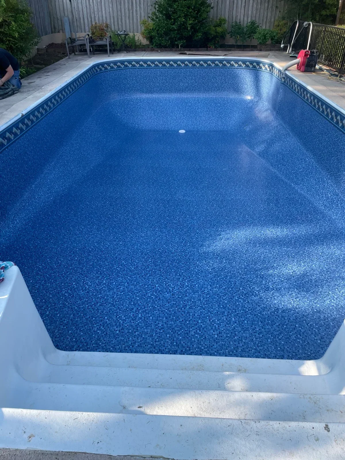 Blue mosaic vinyl pool liner with white coping and decorative border trim in concrete in-ground pool