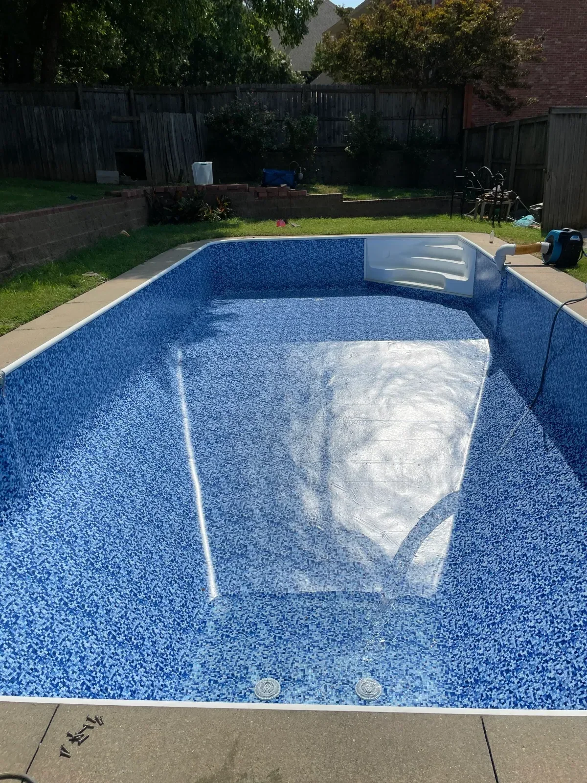 In-ground pool with blue aggregate interior finish, white sun shelf, and concrete deck surround
