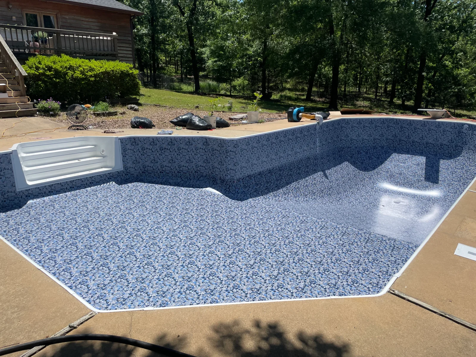 In-ground pool with new speckled blue interior finish, white skimmer, and concrete deck during renovation