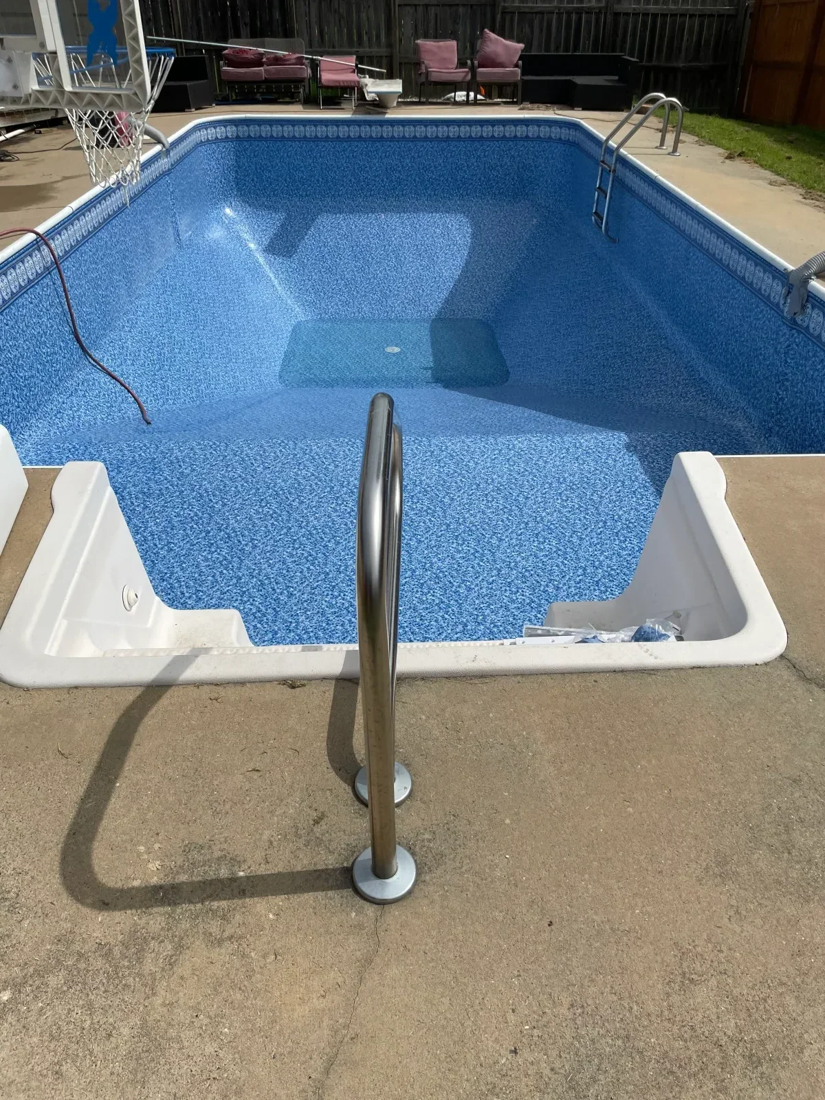 Stainless steel handrail installed on pool deck with blue in-ground pool and white coping visible