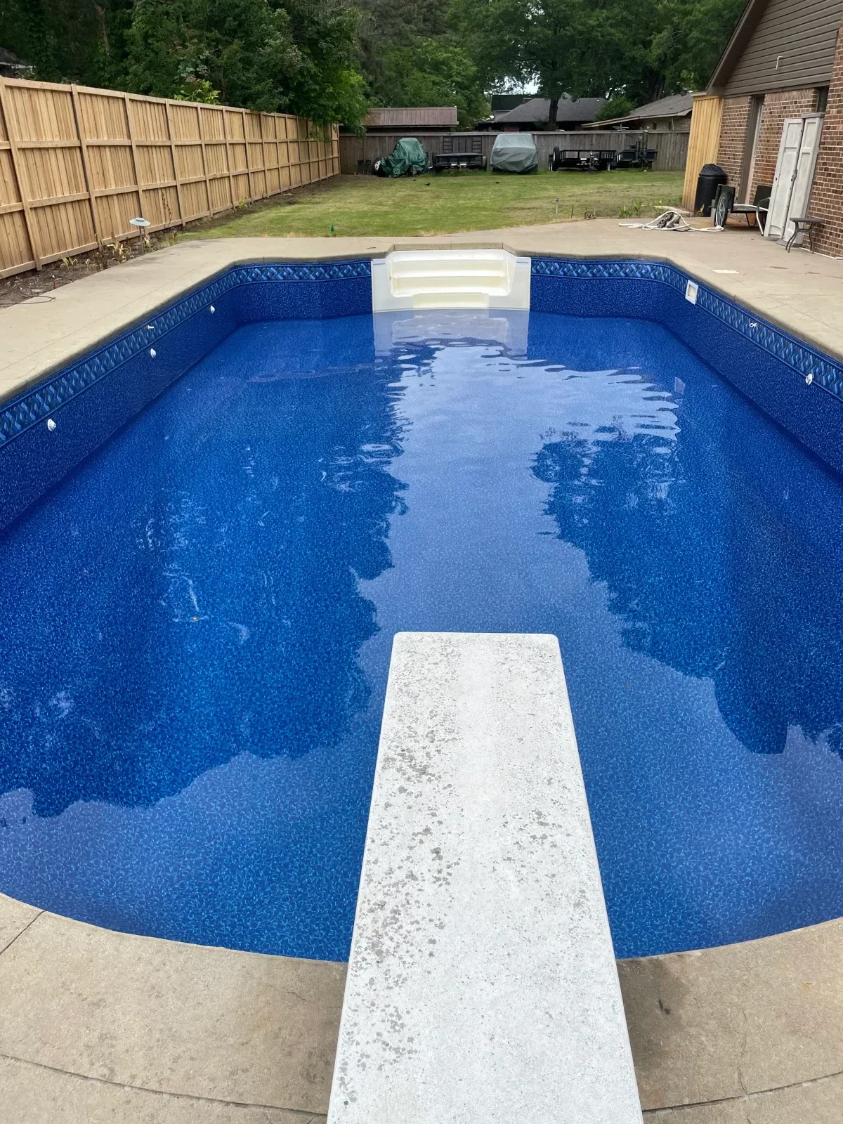 In-ground pool with fresh blue interior finish and white concrete deck during resurfacing project