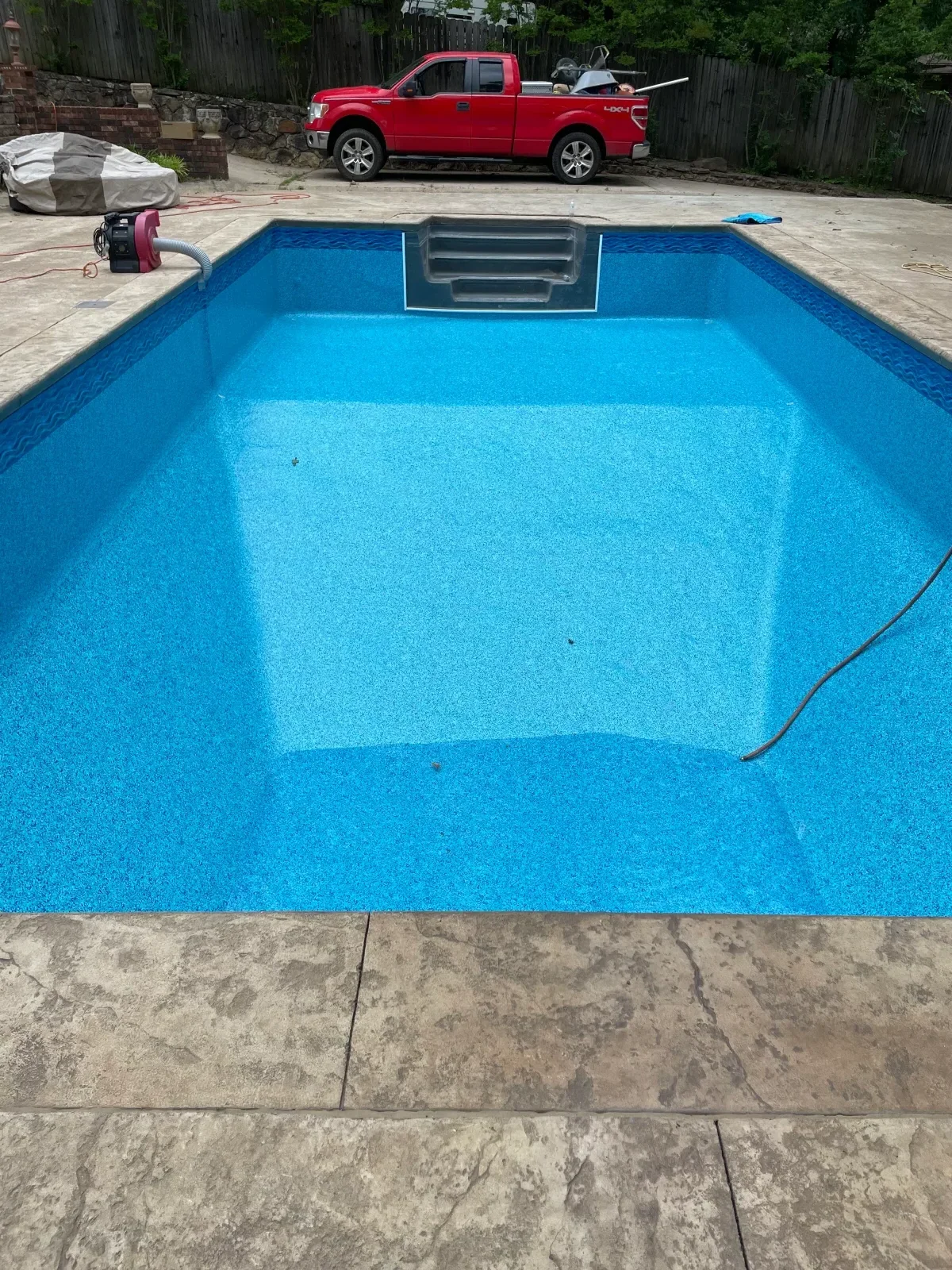 Bright blue in-ground pool with new plaster finish and concrete deck, equipment visible at waterline